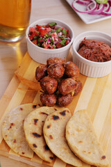 A traditional latin american chorizo links served in a wooden board next to some tortillas and condiments.