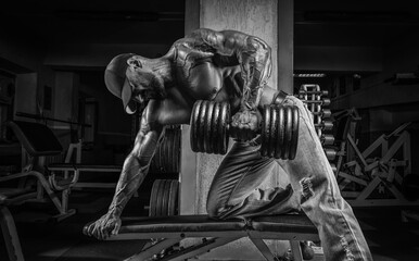 Muscular man pulls a dumbbell towards his stomach. Bodybuilding and powerlifting concept.