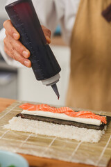 close up chef making sushi. Sushi roll process adds sauce to sushi