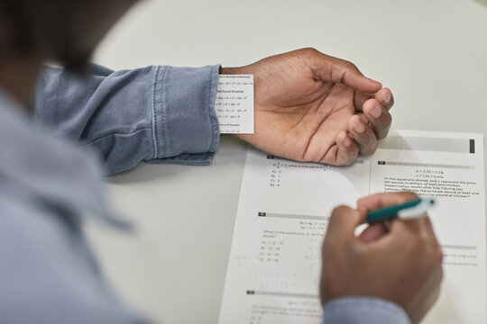 Closeup of unrecognizable student hiding cheat note while taking exam in school, copy space