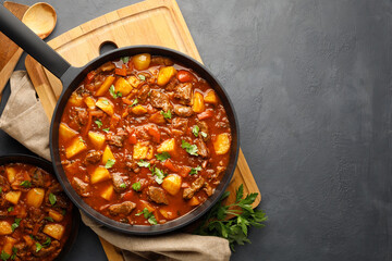 Goulash, beef stew with vegetables in tomato sauce. Top view. Dark (black) background.
