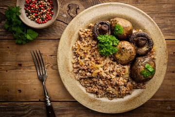 Buckwheat porridge with mushrooms in a plate on wooden table, top view