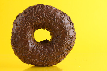 doughnut in chocolate glaze on bright yellow background with a place to stand up the text of the copyspace. No diet day