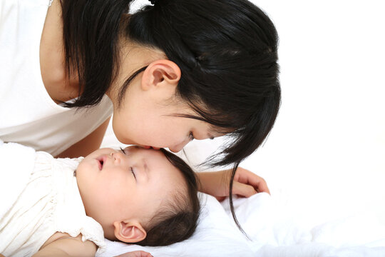 昼寝する赤ちゃんの額にキスするお母さん。母性、愛情イメージ