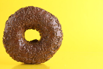 doughnut in chocolate glaze on bright yellow background with a place to stand up the text of the copyspace. No diet day