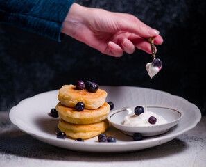 Pancakes are small cheesecakes made by hand with hand serving delicious with berries on a beautiful plate with sour cream and chocolate