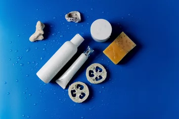 Fotobehang Lotion, mycelium water in a white plastic bottle, tuba for eye care cream, eyelids, soap natural, pieces of loof on a blue background with drops of water, flat layout, copying space © Aleksandra