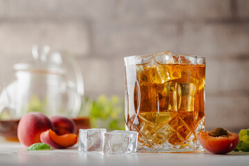 Glass of peach or apricot iced tea with fruit slices against white background