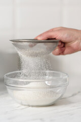 Close-up of a woman's hands sifting flour through a sieve.