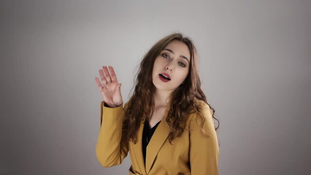 Portrait of young irritated woman making bla bla sign by her hand on white background in a slowmo. A caucasian lady does not believe somebody and gesturing. She is annoyed and sad. Expressing emotions