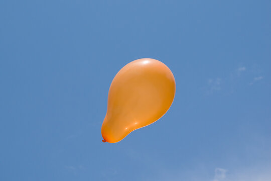 picture of orange balloon flying under blue sky with white clouds.