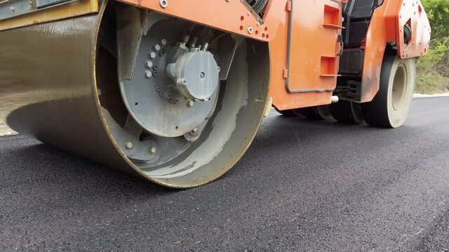Road construction. Asphalt compactor heavy machine working on a fresh hot layer of asphalt, on a rainy day