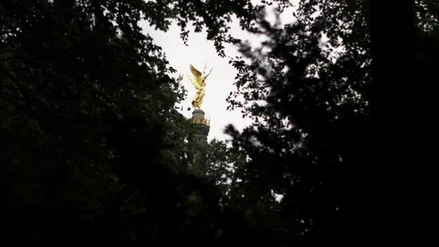 Golden statue among tree branches with sky in the background.