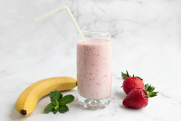 Smoothie with strawberries and banana in a transparent glass, banana, strawberries and mint on a light background. The concept of proper nutrition.