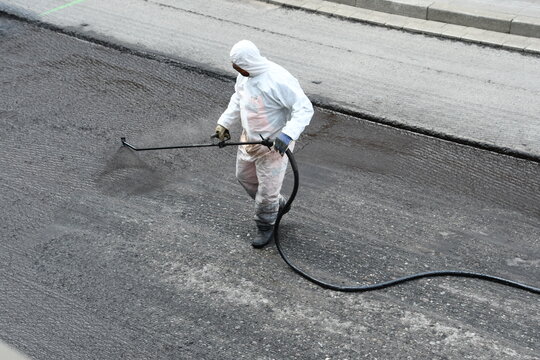 Straßenarbeiter mit weißem Schutzanzug versprüht Bitumen auf Straßenbaustelle