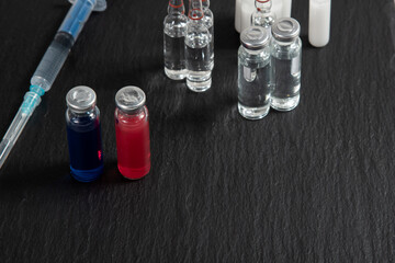 Ampoules with red and blue serum stand on a black background with a syringe and other ampoules