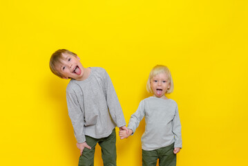 Two cute boys have fun and show their tongues. Studio photography on a colored (yellow) background.