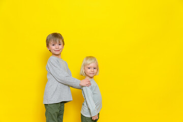 Two little boys in a great mood. The older brother holds his brother by the shoulders. Yellow (colored) background.