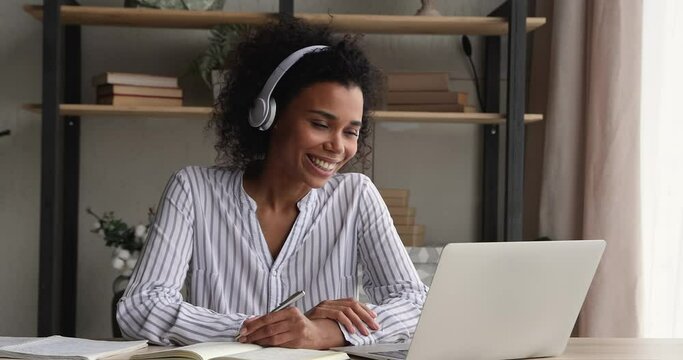 African student woman take part in educational webinar via video call. Female sit at desk wear headphones talk to teacher by videoconference. E-learning event with online tutor, modern tech concept