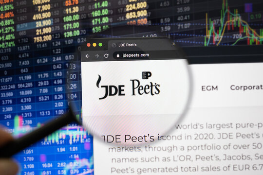 JDE Peet's company logo on a website with blurry stock market developments in the background, seen on a computer screen through a magnifying glass
