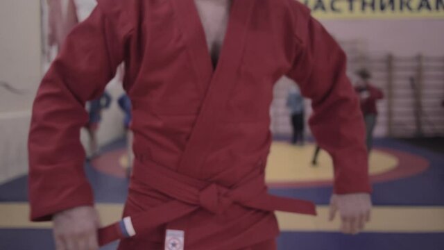 Adult russian wrestler dressed in red kimono tie a red belt before fight. No face. High quality FullHD footage