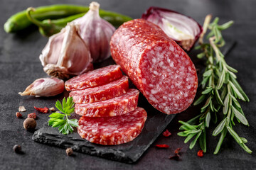 Traditional smoked salami sausage with spices.Salami sausage slices on a black chopping Board. Dark background. - obrazy, fototapety, plakaty
