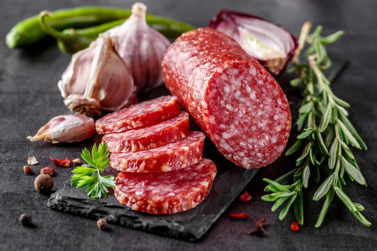 Traditional smoked salami sausage with spices.Salami sausage slices on a black chopping Board. Dark background.