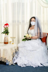 A Jewish bride sits in a synagogue before a chuppa ceremony during a pandemic wearing a medical mask and a bouquet of flowers awaits the groom.