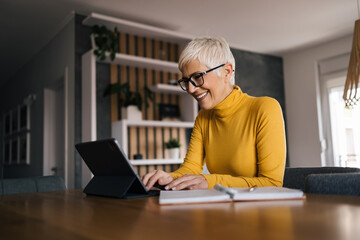 Fototapeta premium Happy senior woman using tablet at home, chatting online.