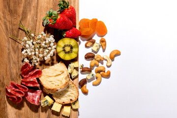 Kiwi, strawberries, cashews, Brazil nuts, apricots, bread, salami and cheese on wooden background. Top view.