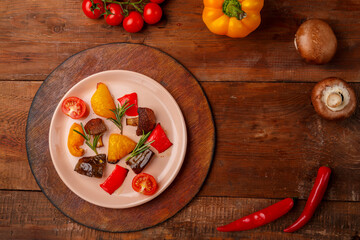Antipasta on a plate on a stand on a wooden table next to fresh bright vegetables.
