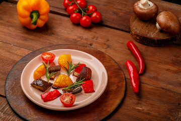 Antipasta on a plate on a stand on a wooden table next to fresh vegetables.