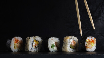 sushi set in a row on a stone board with chopsticks on a dark plaster background. artistic moody food photo with copy space