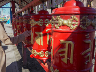 buddhist prayer drums in red with golden hieroglyphs, a woman's hand touches them