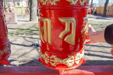 buddhist prayer drums in red with golden hieroglyphs, a woman's hand touches them
