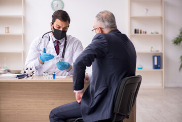 Old businessman visiting young male doctor in vaccination concep
