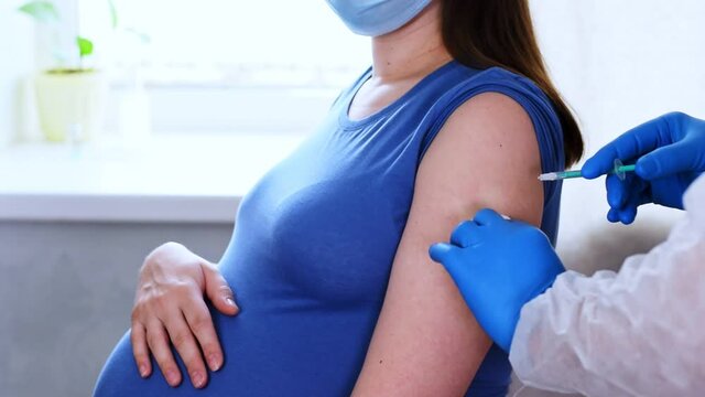 Pregnant Vaccination. Doctor giving COVID -19 coronavirus vaccine injection to pregnant woman. Doctor Wearing Blue Gloves Vaccinating Young Pregnant Woman In Clinic. People vaccination concept. Slow