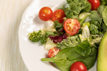 White dish with fresh leaf salad, cherry tomatoes, cucumber and avocado. Proper balanced detox diet.