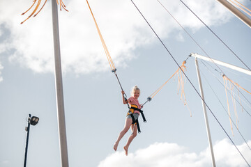A girl of about 8 years old is jumping on a bungee trampoline. A child with a harness and elastic...