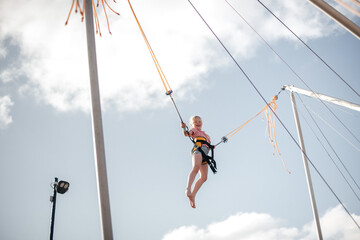 A girl of about 8 years old is jumping on a bungee trampoline. A child with a harness and elastic...
