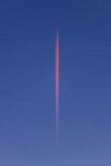 plane in the blue sky at sunrise - behind the plane a red streak of water vapor