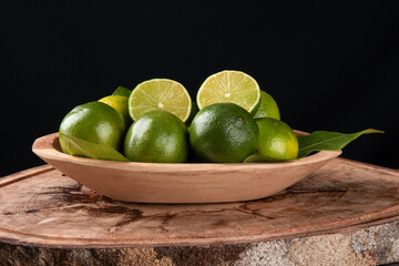 Green lime fruit in wooden bowl and black background