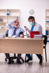 Young male doctor visiting old businessman at workplace