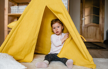 a little girl plays inside a yellow teepee