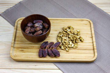 Fruit dates fruits. A bunch of walnut kernels. A sprig of date fruit with a wooden bowl of date fruit and a walnut kernel on a wooden tray.