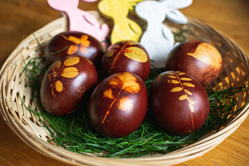 Obraz premium Easter eggs coloured using the old technique with onion skin and stockings. Traditional and organic way of colouring eggs. Eggs are in a basket with grass with. Decorated with wooden easter bunnies