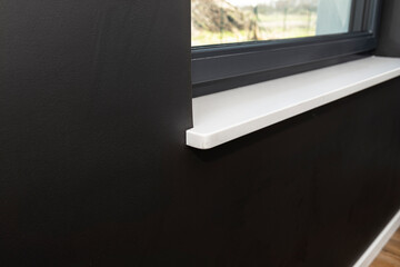 Newly installed white conglomerate window sill inside the room, on the black wall. - obrazy, fototapety, plakaty