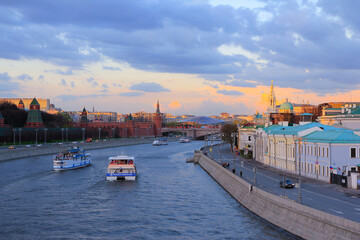 Blue-yellow sunset in Moscow with a view of old buildings along the embankments of the Moskva River and excursion boats.