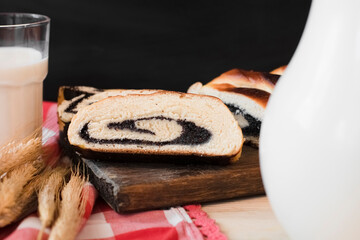 Baked roll with poppy seeds, glass decanter and glass cup with milk, close up