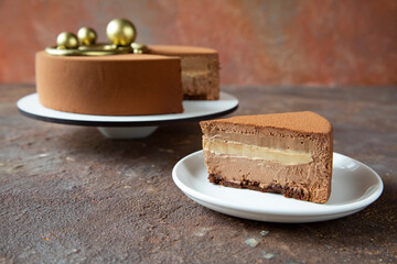 A piece of chocolate mousse cake on the background of a large cake decorated with golden spheres - the concept of a festive dessert for a birthday or Christmas